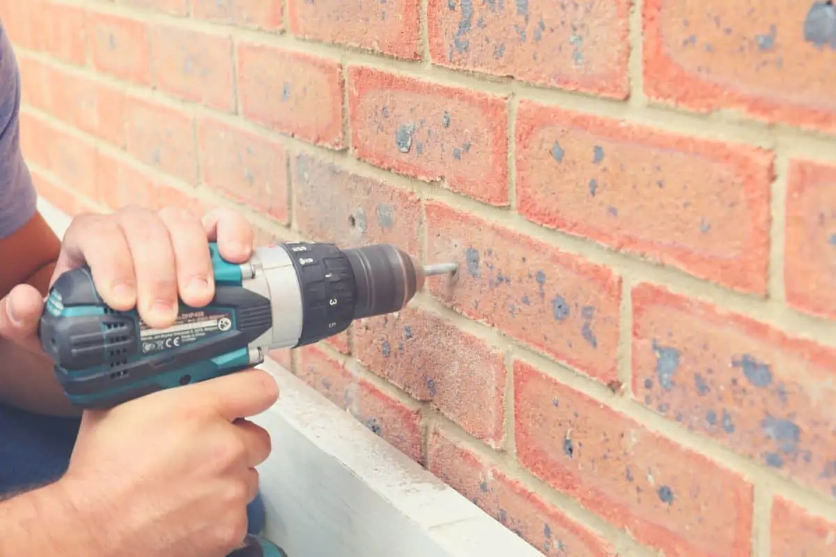 A man drilling a hole into a brick wall with a hammer drill and masonry drill bit