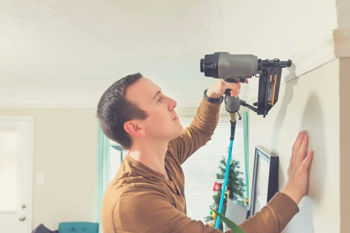 A man fitting some wall trim with a brad nailer