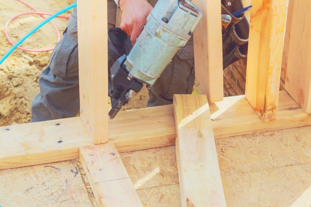 A construction worker erecting a timber frame with a framing nailer