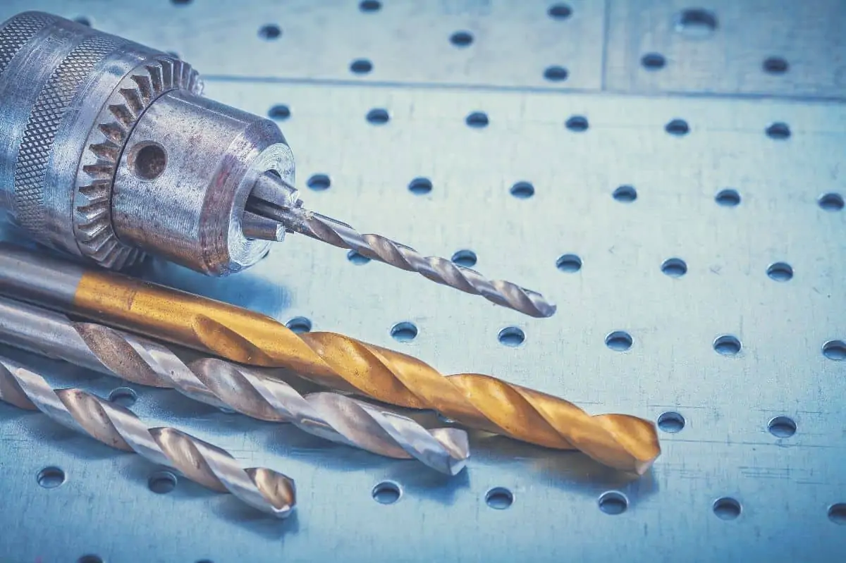 A collection of titanium and cobalt drill bits with a cobalt drill bit in a drill chuck
