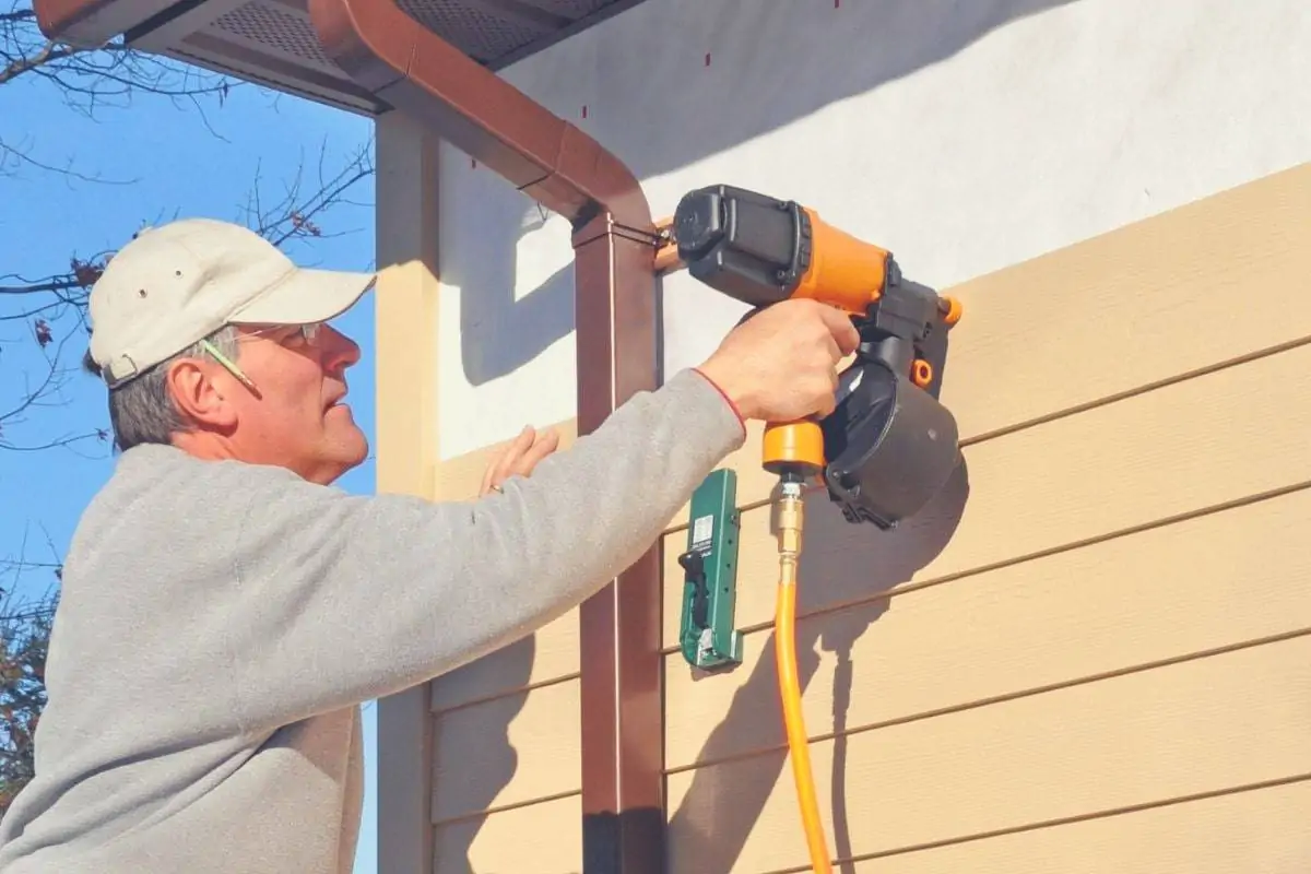 A man using a siding nail gun to install wooden siding to a house. 