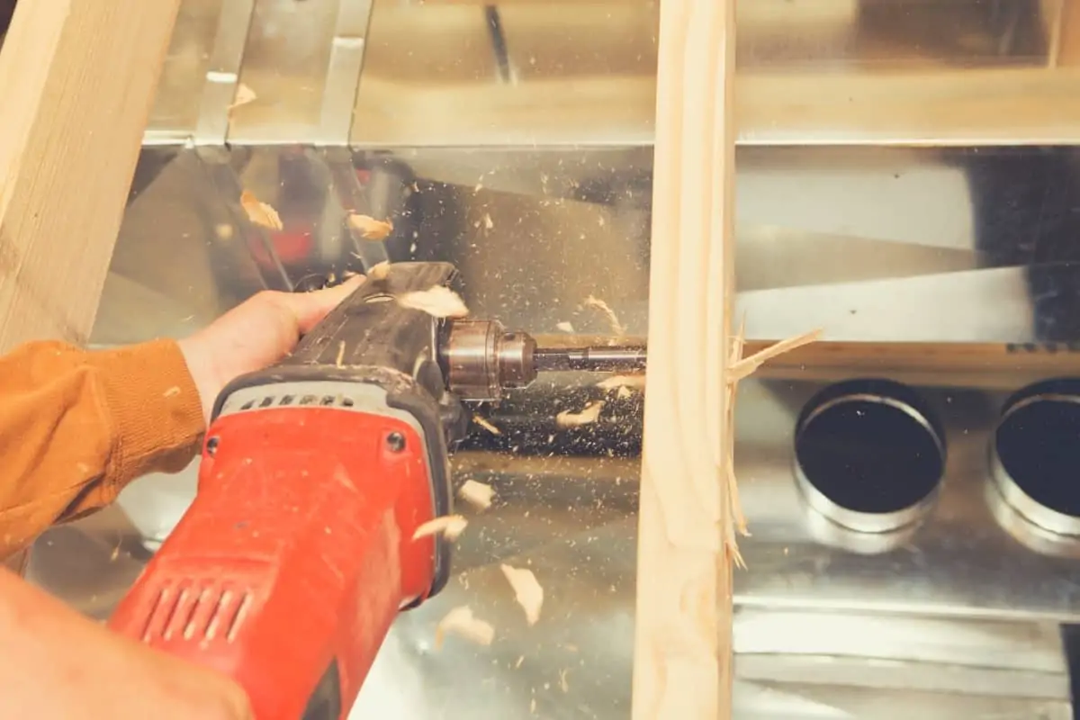 A carpenter drilling a hole in some tight framing using a right angled drill