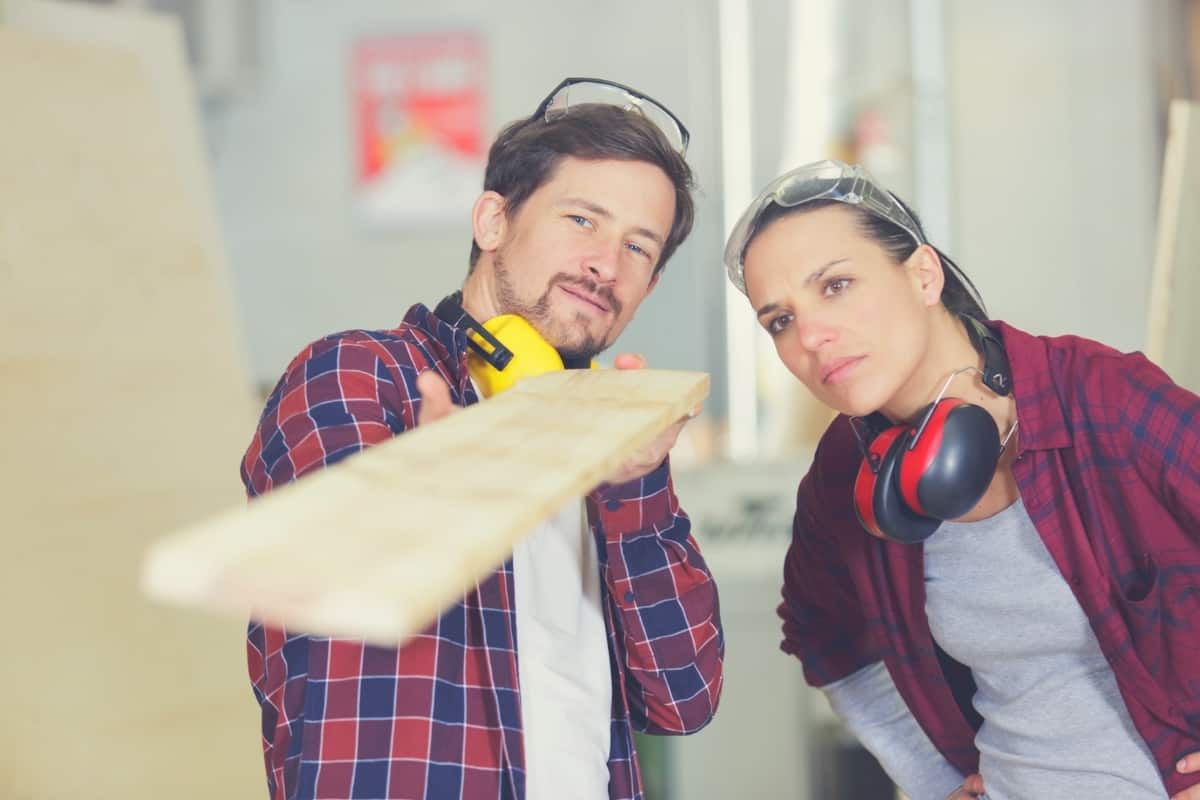 A male and a female carpenter checking to see if a piece of wood is straight