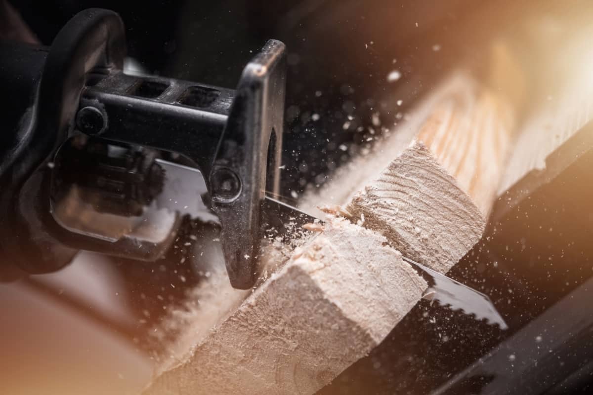 A close up of someone cutting wood with a cordless reciprocating saw